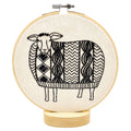 The Sweater Weather Sheep Complete Embroidery Kit by Hook, Line & Tinker features a black and white geometric sheep on a wooden base—perfect for embroidery lovers seeking a whimsical craft project.