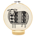 The Sweater Weather Sheep Complete Embroidery Kit by Hook, Line & Tinker features a black and white geometric sheep on a wooden base—perfect for embroidery lovers seeking a whimsical craft project.