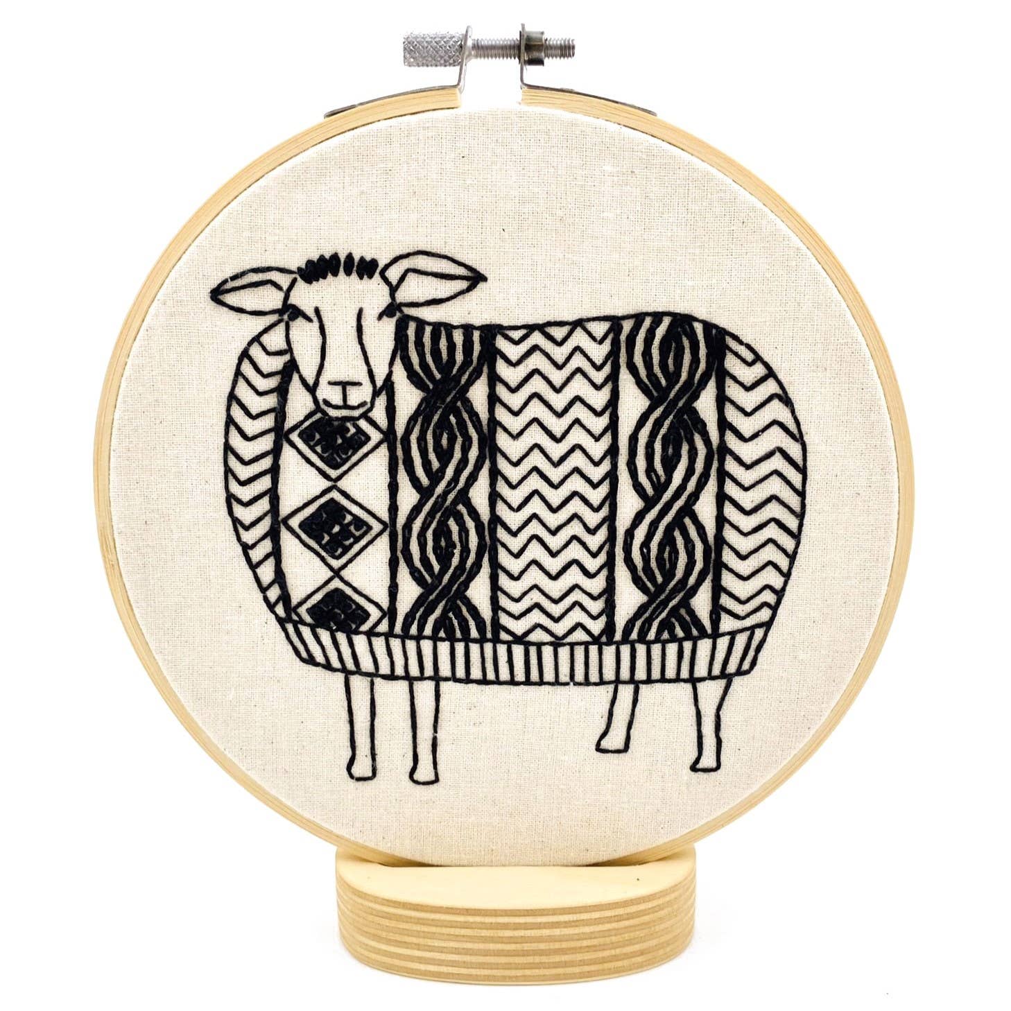 The Sweater Weather Sheep Complete Embroidery Kit by Hook, Line & Tinker features a black and white geometric sheep on a wooden base—perfect for embroidery lovers seeking a whimsical craft project.
