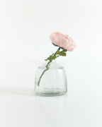 A single light pink flower with green leaves is displayed in the Bella Handblown Hammered Glass Bud Vase: Blush by Creative Women, set against a plain white background.
