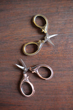 The Mini Embroidery Scissors: Antique Gold by NNK Press feature ornate handles and sharp stainless steel blades. These compact sewing snips are perfect travel notions for any sewing enthusiast and sit elegantly on any work surface.
