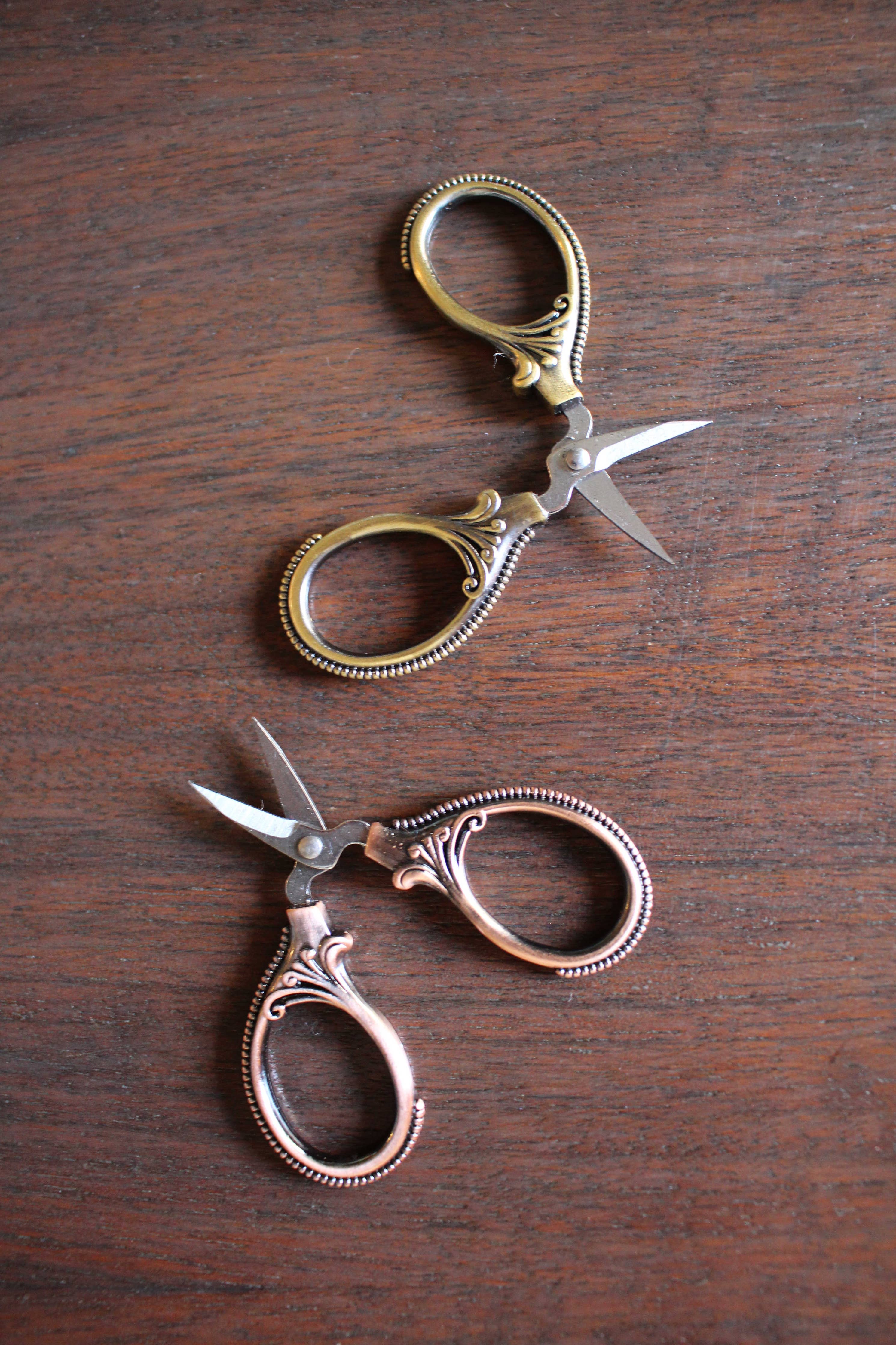 The Mini Embroidery Scissors: Antique Gold by NNK Press feature ornate handles and sharp stainless steel blades. These compact sewing snips are perfect travel notions for any sewing enthusiast and sit elegantly on any work surface.