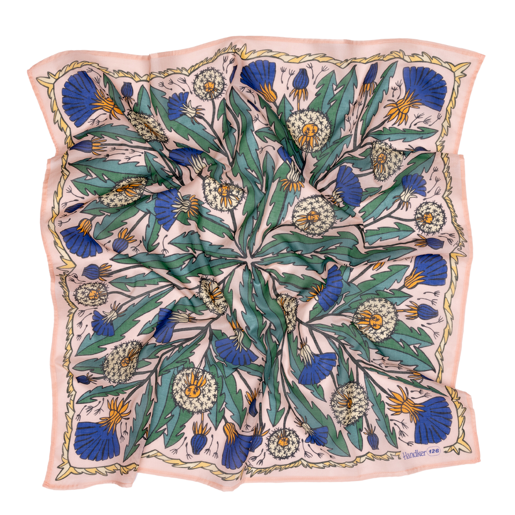 The 34" Dandy Wild Rag Bandana by Handker Bandanas is a square silk scarf with a botanical print of dandelions, green leaves, and blue thistles on pale pink, bordered with wavy lines and inspired by classic bandanas. Fabric has a slightly rumpled look.