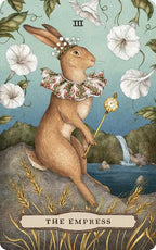 A majestic rabbit adorned with a crown and ruffled collar clasps a scepter amid white flowers, wheat, and a cascading waterfall on this nature-inspired tarot card from Tarot of the Woodland Wardens by Jessica Roux (Simon & Schuster). The card features The Empress and the Roman numeral III.