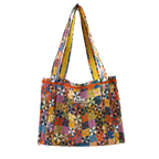 The Calico Quilted Tote by Handker Bandanas features a geometric pinwheel quilt pattern in bright colors, two shoulder straps, and a small kinder label on the front against a plain white background.