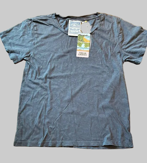 A Thyne Goods Ojai Tee in Diesel Grey, made from a hemp cotton blend with short sleeves, is laid flat on a gray background. Tags are attached near the collar, one displaying the text FEAR LOVE.
