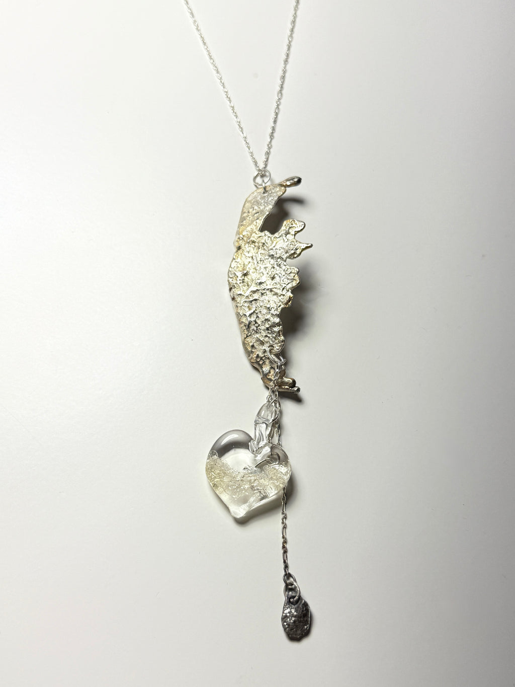 The Wing Fall necklace by Thyne Goods (Ash Espinoza x Thyne Studio) features an abstract textured pendant, a handmade glass heart with silver, and a small dangling charm, all shown on a white background.