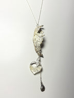 The Wing Fall necklace by Thyne Goods (Ash Espinoza x Thyne Studio) features an abstract textured pendant, a handmade glass heart with silver, and a small dangling charm, all shown on a white background.