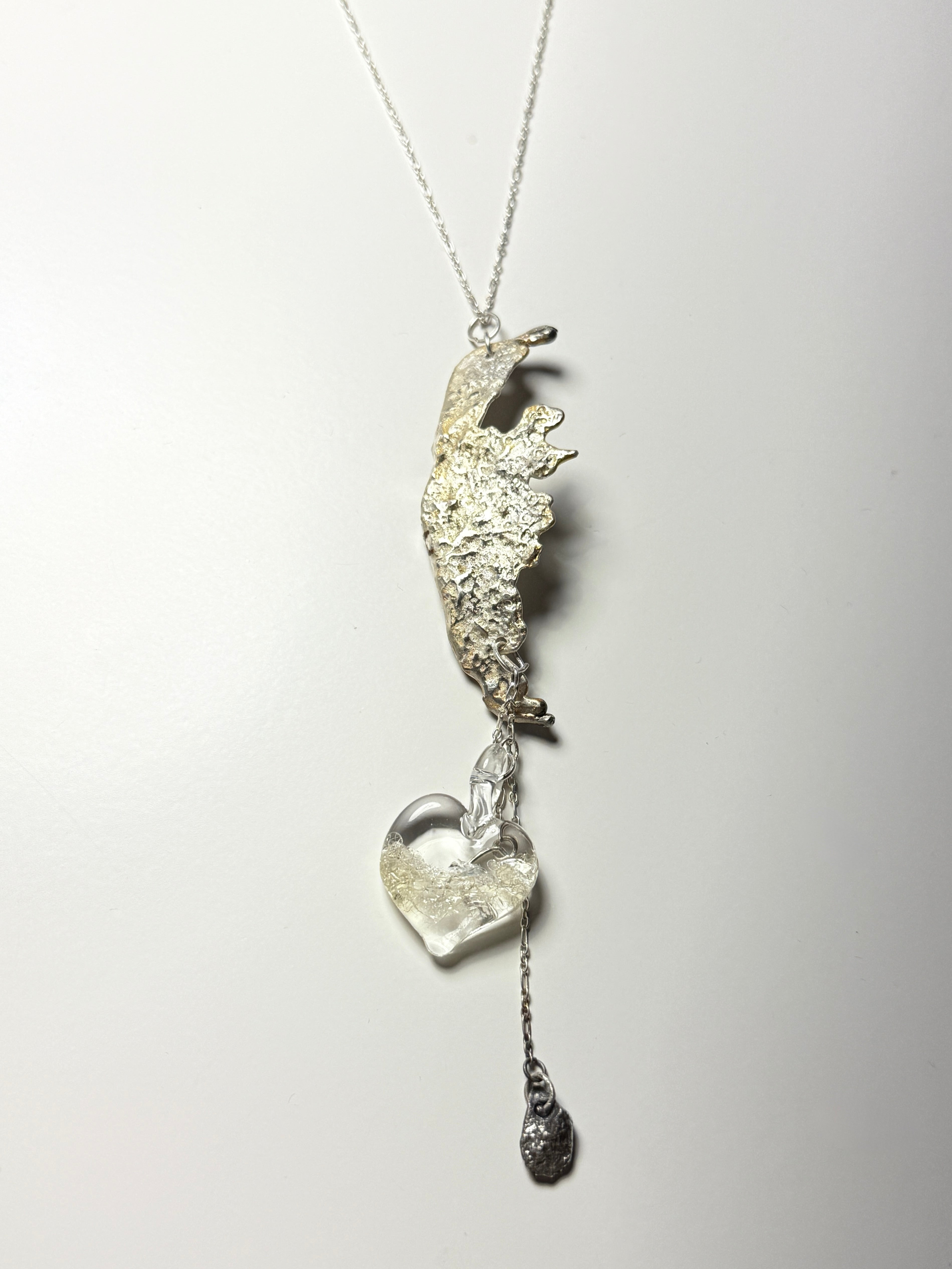 The Wing Fall necklace by Thyne Goods (Ash Espinoza x Thyne Studio) features an abstract textured pendant, a handmade glass heart with silver, and a small dangling charm, all shown on a white background.