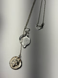 The Trickster • Ash Espinoza x Thyne Studio necklace by Thyne Goods features a sterling silver chain with a heart-shaped clasp, a clear handmade glass heart pendant, and a round wolf head charm, displayed on a smooth gray surface.